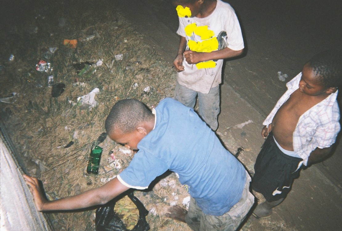 Drei Kinder spielen im Dreck und zerbrechen Flaschen. Gefährlich und unsicher.