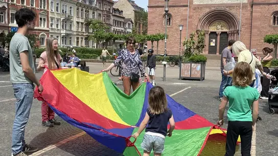 En Wilhelmsplatz, frente a una iglesia en Heidelberg Weststadt, miembros Terre des Hommes , otros participantes y niños sostienen un gran paracaídas de colores y juegan.