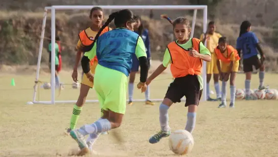 Mädchen in Indien spielen Fußball auf einem Feld, tragen bunte Trikots und zeigen Begeisterung und Teamgeist.