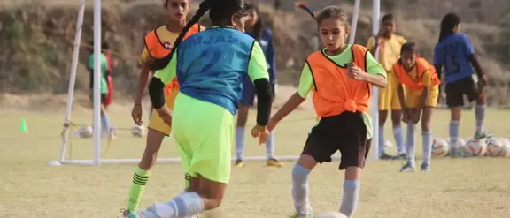 Mädchen in Indien spielen Fußball auf einem Feld, tragen bunte Trikots und zeigen Begeisterung und Teamgeist.