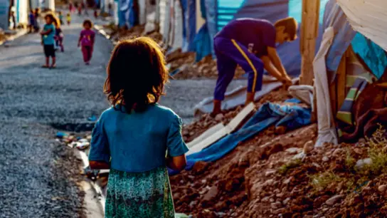 Kind steht in einer Gasse eines Fluchtcamps. Claim: Sichere Wege - Zuflucht für Kinder