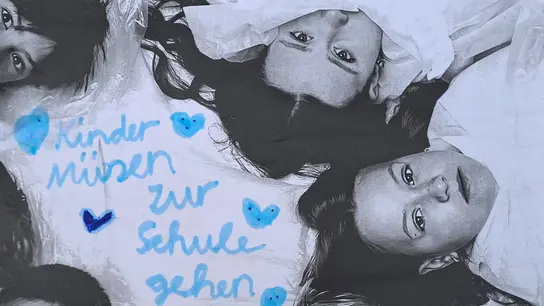 Kinderliegen im Kreis um einen Schriftzug "Kinder müssen zur Schule gehen", mit den Köpfen zur Mitte