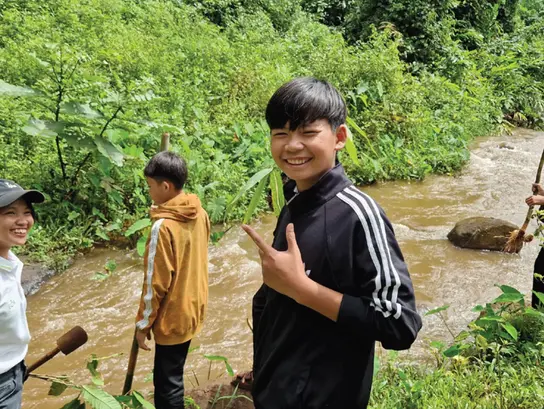 Tres adolescentes plantando bambú junto a un cuerpo de agua