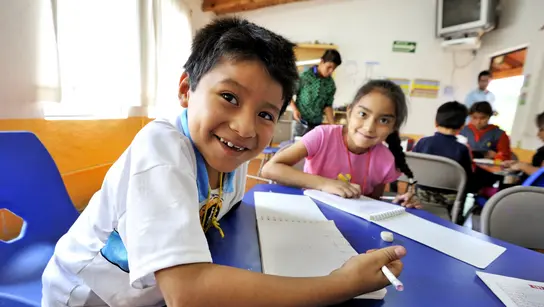 Ein Junge und ein Mädchen arbeiten an einem blauen Tisch, im Hintergrund sind weitere Kinder
