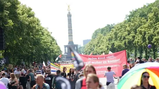 Menschen mit Schildern bei einer Demonstration und ein Banner mit der Aufschrift "Jedes Kind Zählt"