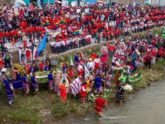 Menschen in andiner Tracht stehen an einem Flussufer