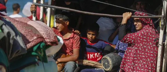 Niños y una mujer se sientan juntos en la parte trasera de un vehículo cargado de mantas y equipaje: refugiados de Gaza en una emergencia humanitaria.