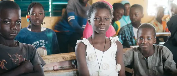  Los niños en un salón de clases en Burkina Faso se sientan con una sonrisa y atentos en sus mesas.