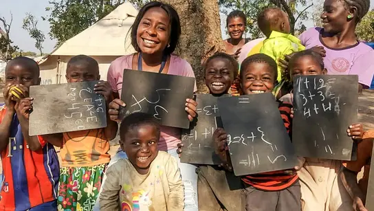 Mehrere Kinder und zwei Frauen lachen glücklich und einige halten Tafeln mit Rechenaufgaben in das Bild
