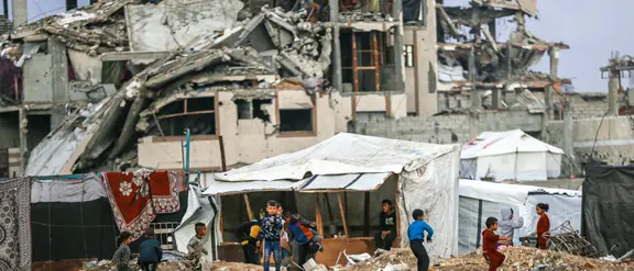 Eine Trümmerlandschaft in Gaza. In der Mitte des Bildes sind spielende Kinder aus der Ferne zu sehen.