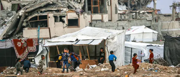 Eine Trümmerlandschaft in Gaza. In der Mitte des Bildes sind spielende Kinder aus der Ferne zu sehen.