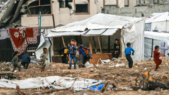 Eine Trümmerlandschaft in Gaza. In der Mitte des Bildes sind spielende Kinder aus der Ferne zu sehen.
