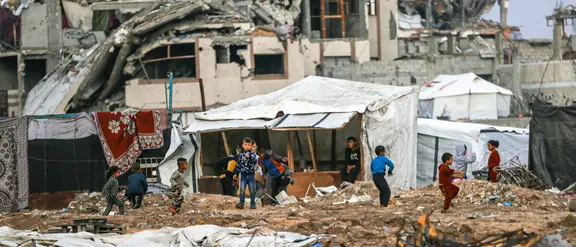 A landscape of rubble in Gaza. In the center of the picture, children playing can be seen in the distance.