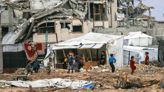 Eine Trümmerlandschaft in Gaza. In der Mitte des Bildes sind spielende Kinder aus der Ferne zu sehen.