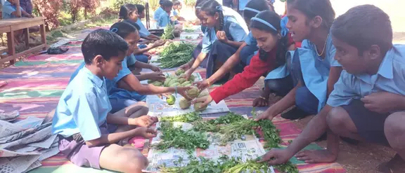 Los niños de la escuela india con uniformes azules se sientan al aire libre y clasifican vegetales frescos juntos en coloridas mantas.