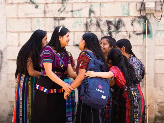 Sechs junge Frauen aus Guatemala stehen draußen in einem Kreis und umarmen sich und lachen dabei.