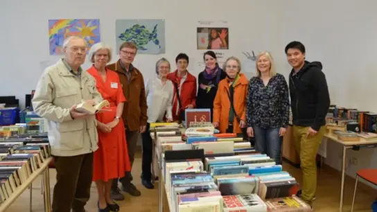Volunteers pose for a group photo. They are surrounded by rows of boxes of books.