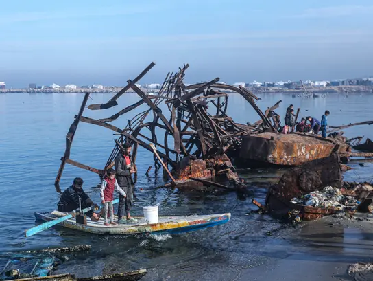 Two fishermen and a child on a boat in front of a shipwreck at sea