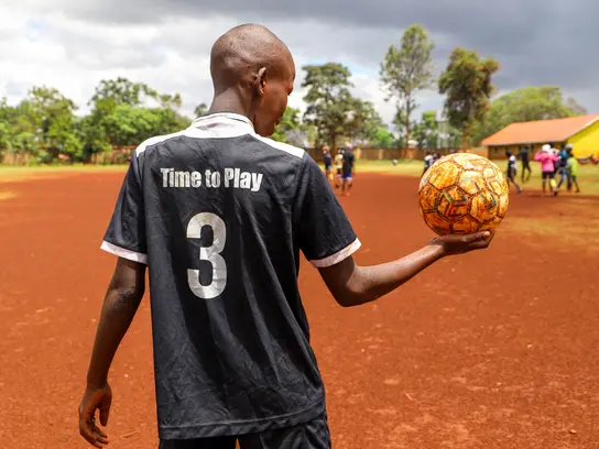 Ein Kind steht vor einem Spielfeld und hält einen Ball fest