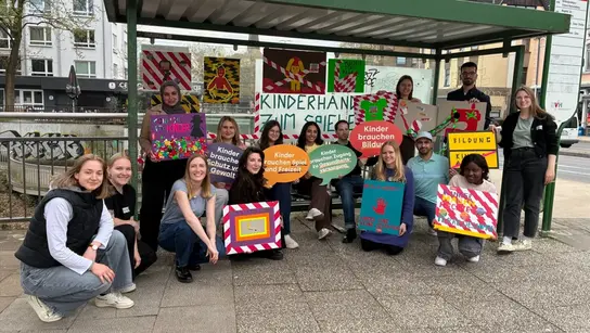 Gruppenfoto der jungen Engagierten von TDH. Sie posen in einer Bushaltestelle mit selbstgemachten Tape-Art Plakaten und Motiven.