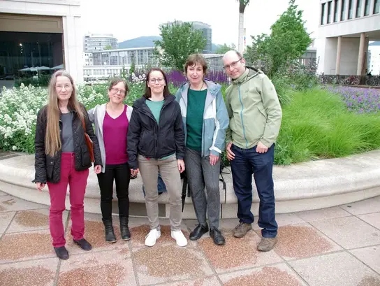 Cuatro mujeres y un hombre posan uno al lado del otro frente a un gran macizo de flores de colores, mirando a la cámara. Se trata de una foto de grupo del colectivo Terre des Hommes en Heidelberg y Mannheim.