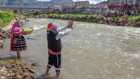 EIn Mann und eine Frau stehen an einem Flussufer und halten ein andines Ritual ab