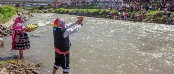 EIn Mann und eine Frau stehen an einem Flussufer und halten ein andines Ritual ab