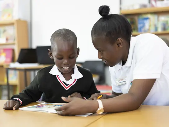 A woman and a child are sitting at a table in front of a book; the woman is explaining something