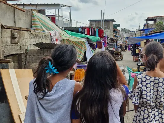 Three girls are walking through a poorer neighborhood.