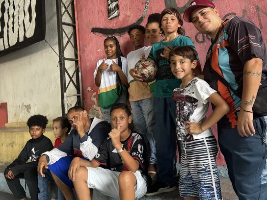 Eine Gruppe Kinder steht mit einem Fußball vor einer bemalten Wand, einige zeigen einen Daumen nach oben  