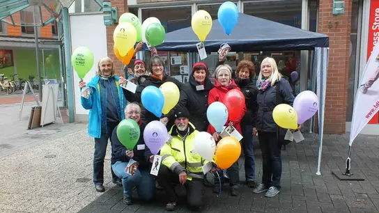 Ehrenamtliche der Terre des Gruppe-Delmenhorst stehen vor einem Pavillon zu einem Gruppenbild mit Luftballons in der Hand.