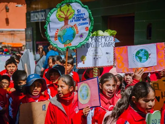 Kinder aus Bolivien demonstrieren mit Schildern in der Hand und roter Kleidung für Kinderrechte.