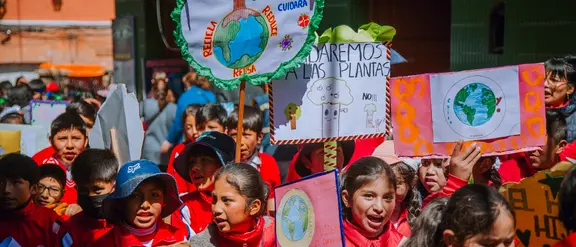 Kinder aus Bolivien demonstrieren mit Schildern in der Hand und roter Kleidung für Kinderrechte.