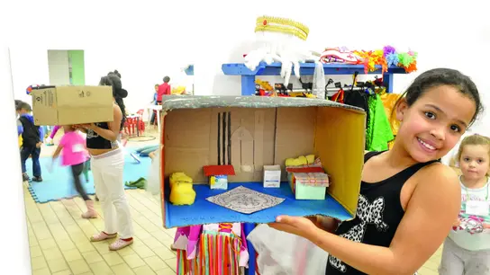 | © D. Mansur Mädchen hält ein selbstgebasteltes Diorama aus einem Karton in einer Ludothek in Brasilien und lächelt stolz.