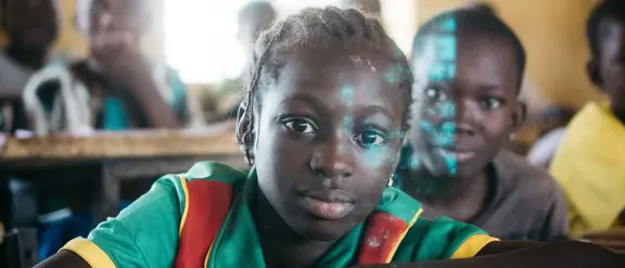 Ein aufmerksames Mädchen sitzt in einem Klassenzimmer in  Burkina Faso. Die Szene zeigt die Bedeutung von Bildung und die Hoffnung auf eine bessere Zukunft durch Lernen.