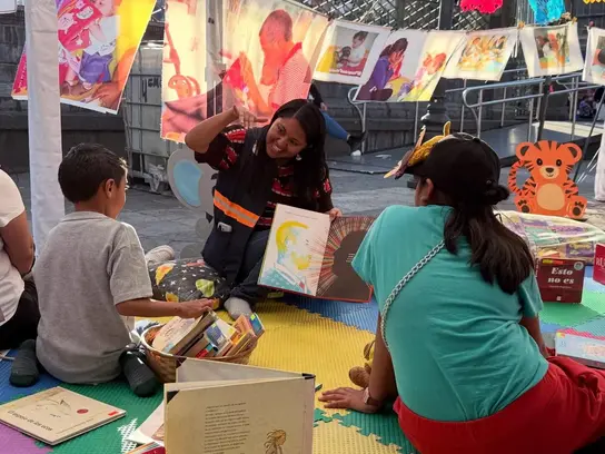 Eine Frau zeigt Kindern lächelnd ein aufgeklapptes Buch