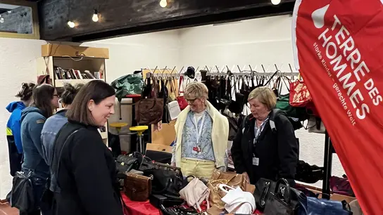 Stand mit Taschen. Ehrenamtliche verkaufen Taschen an einem TDH-Stand.