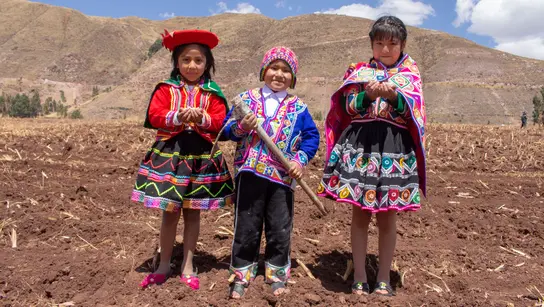 Drei Kinder stehen in traditioneller Kleidung vor einem Feld 