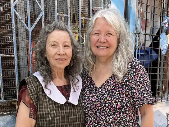 Two older women are standing in front of a wall