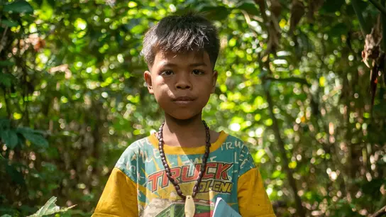 A little boy stands in the forest with a notebook