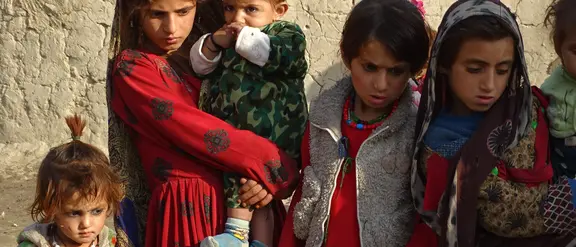 Eine Gruppe von Kindern in bunter, traditioneller Kleidung steht vor einer lehmigen Wand.