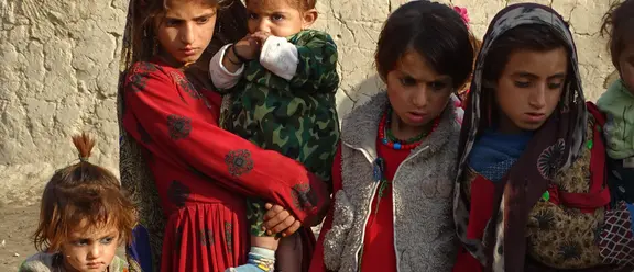 Un grupo de niños con ropa colorida y tradicional se encuentra frente a una pared llorosa.
