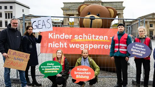 Eine Gruppe von Menschen mit Schildern und einem Riesenteddy steht vor dem Brandenburger Tor