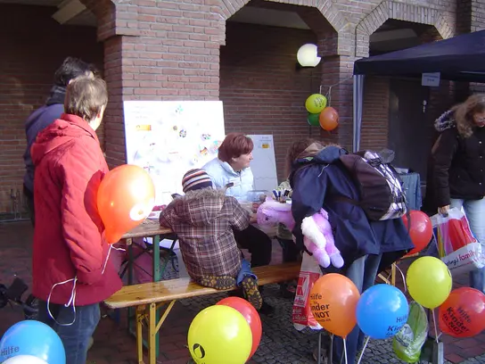 Ein bunt dekorierter Aktionsstand mit Ballons und einigen Besucher*innen