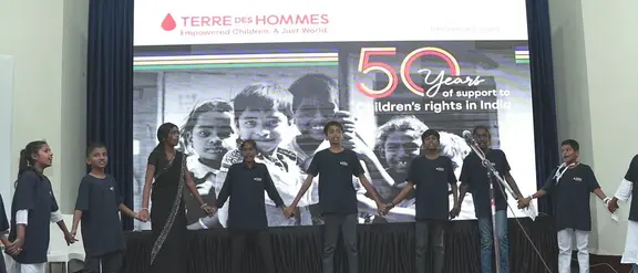 Zwölf indische Kinder stehen in einer Reihe auf einer Bühne und halten sich an den Händen zur 50-Jahre-Feier von Terre des Hommes