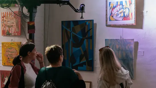 Das Bild zeigt Besucher*innen der Kunstroute Ehrenfeld bei der Kunstaktion der Terre des Hommes Gruppe Köln vor ausgestellten Kunstwerken