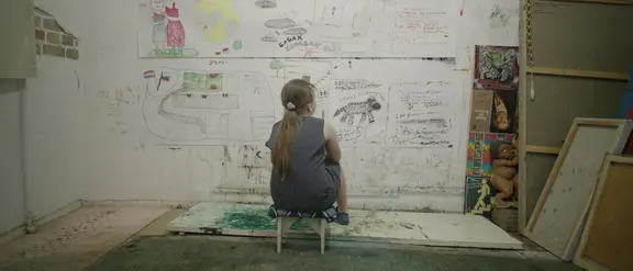Ein kleines Mädchen sitzt vor einer Wand mit Zeichnungen