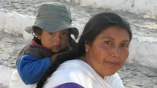 In Guatemala trägt eine Mutter ihr Kind auf dem Rücken, während sie auf einer steinernen Treppe sitzt. Die Szene zeigt die enge Bindung und traditionelle Lebensweise in der Region.
