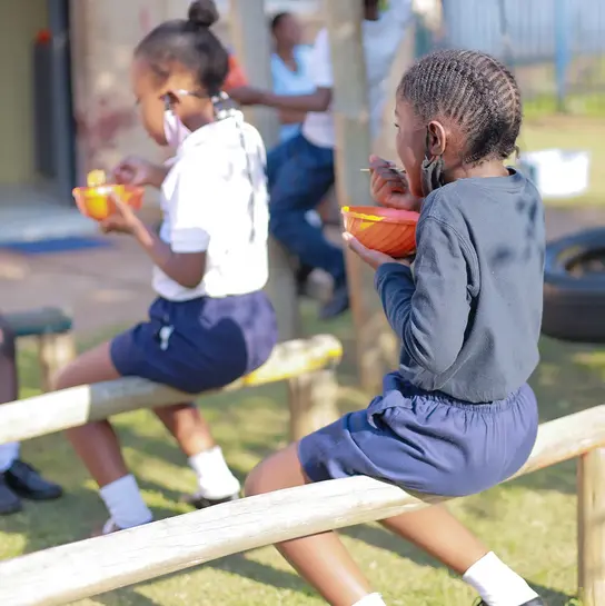 Südafrika: Zwei Kinder sitzen hintereinander und essen. 