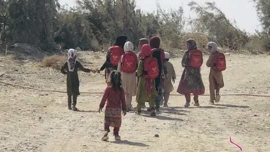 Los niños con mochilas rojas van por un camino polvoriento a lo largo de una zona rural en su camino a la escuela.